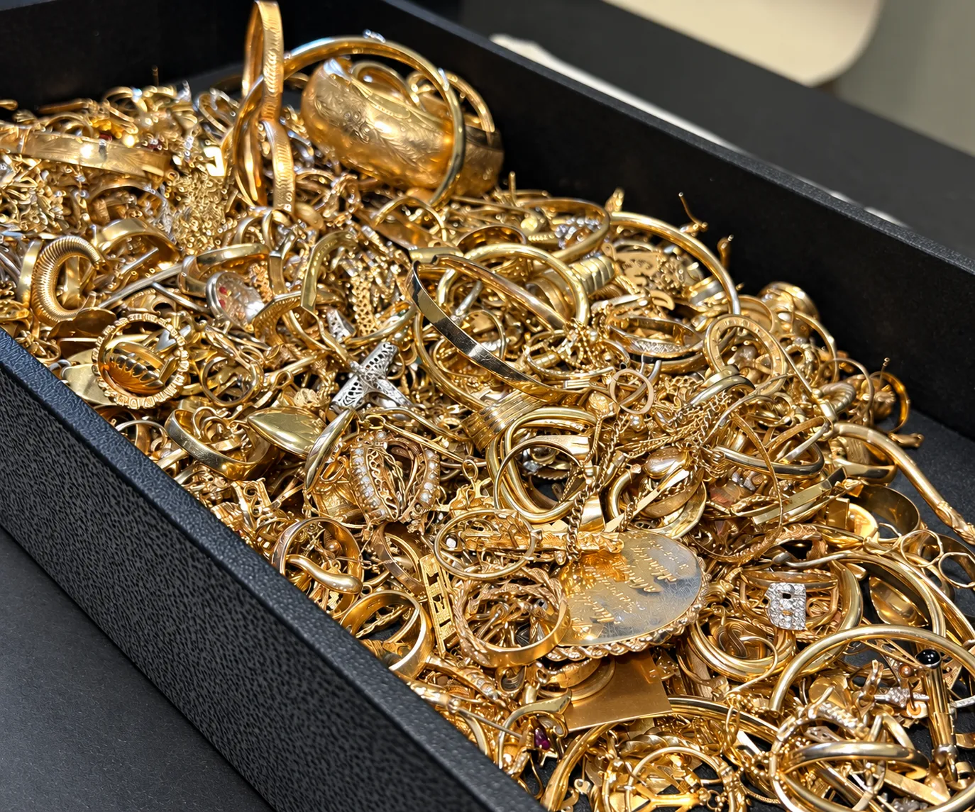 Bandeja negra llena de prendas de oro: pulseras, argollas, anillos, cadenas, medallas y una cruz.